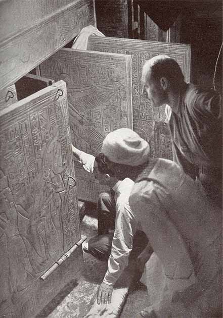 Howard Carter (kneeling), Arthur Callender, and an Egyptian workman in the burial chamber, looking through the open doors of the four gilded shrines towards the quartzite sarcophagus of Tutankhamun. (Public domain)